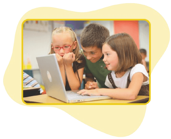 Three children gathered around a laptop, smiling and collaborating in a classroom.